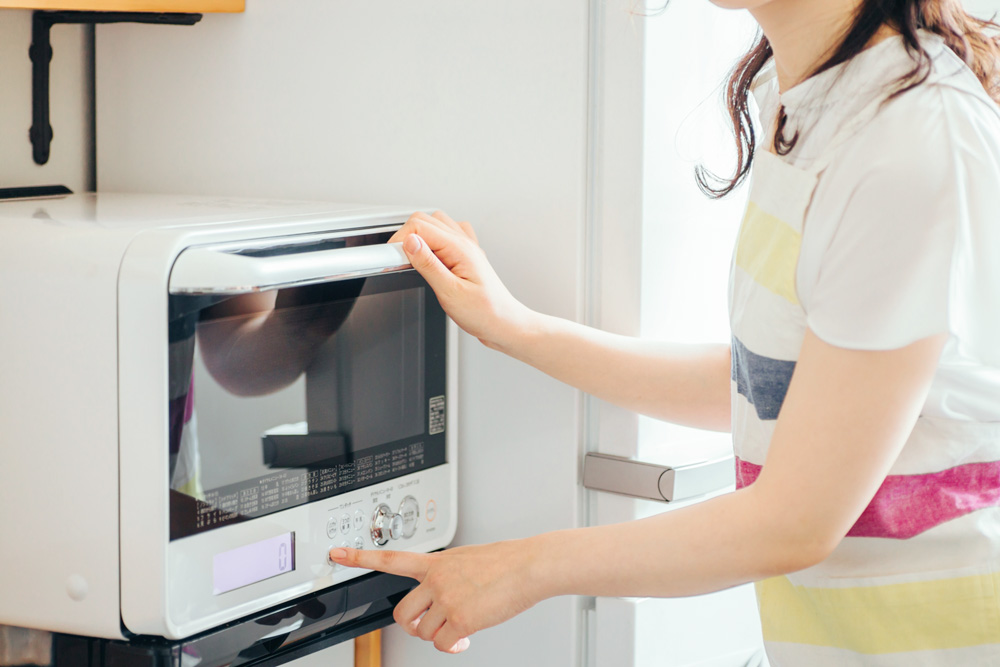 キッチンの電子レンジと女性の画像