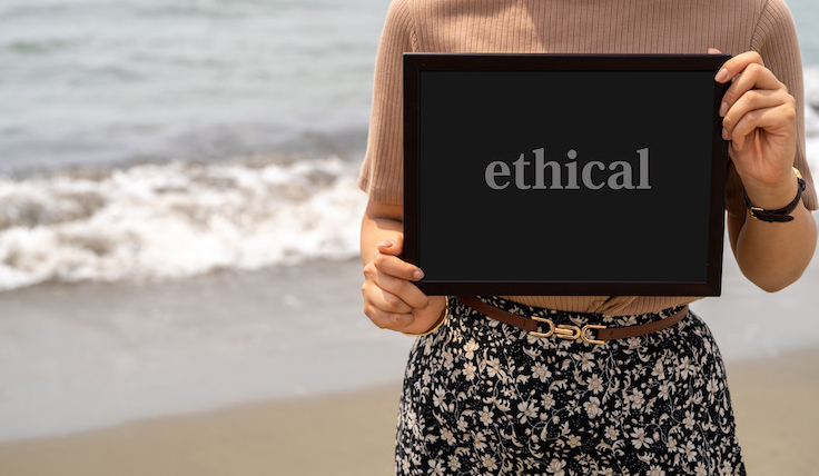 浜辺でエシカルのプレートを持った女性